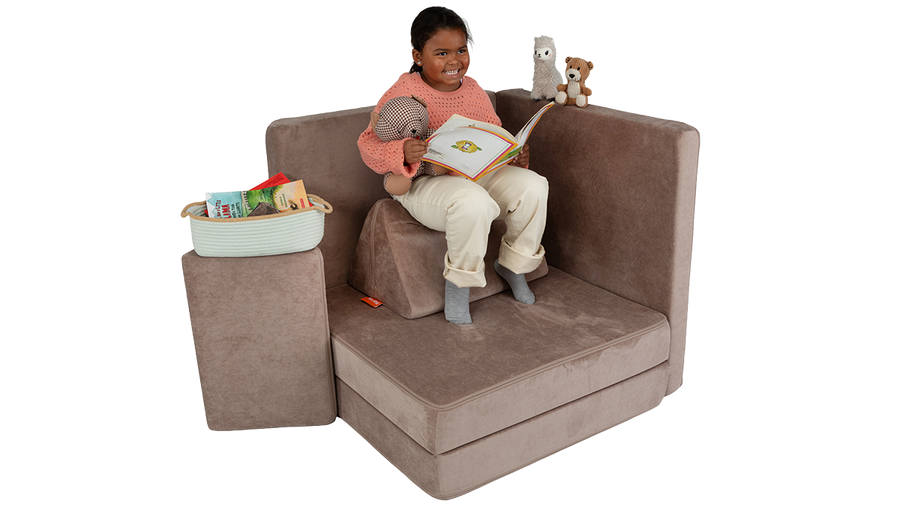 A child reads a book while cozied up in a reading nook made from a taupe Nugget play couch.