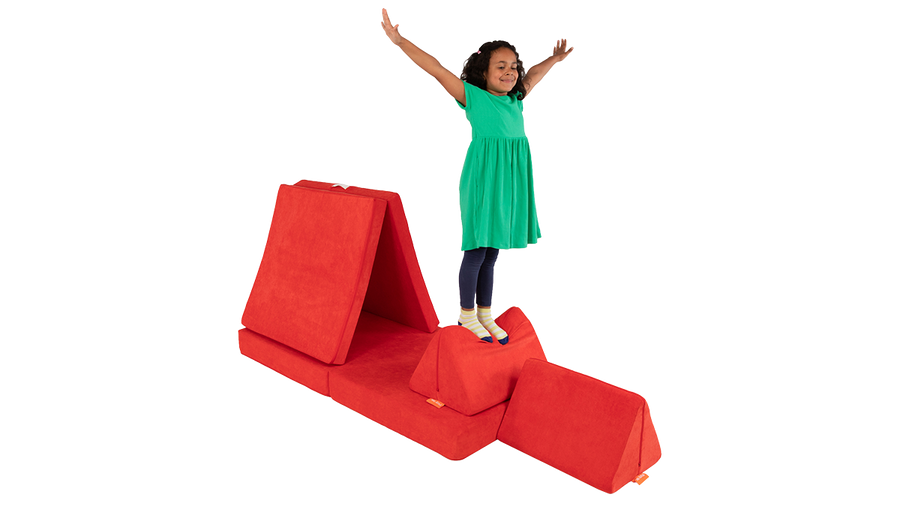 A child strikes a fun pose while standing on the pillow of a poppy red Nugget play couch.