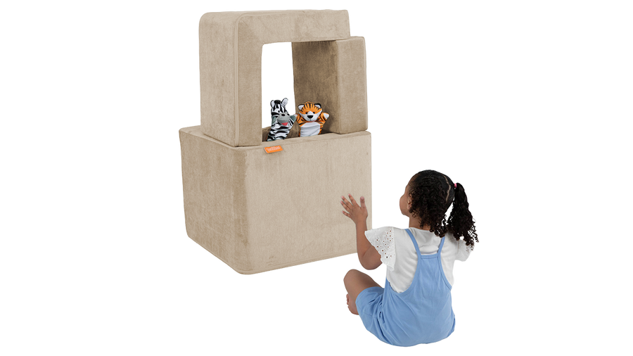 A child watches a puppet show in a mini theater built from the pieces of a beige Smore play chair.