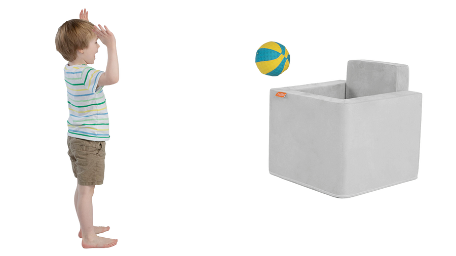 A child tosses a ball into a large basket made from the pieces of a light gray Koala Smore play chair.