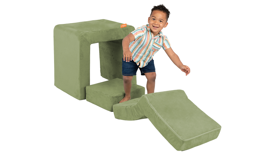 A child climbs the elbow piece of a sage green Smore play chair.