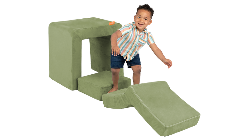 A child climbs the elbow piece of a sage green Smore play chair.
