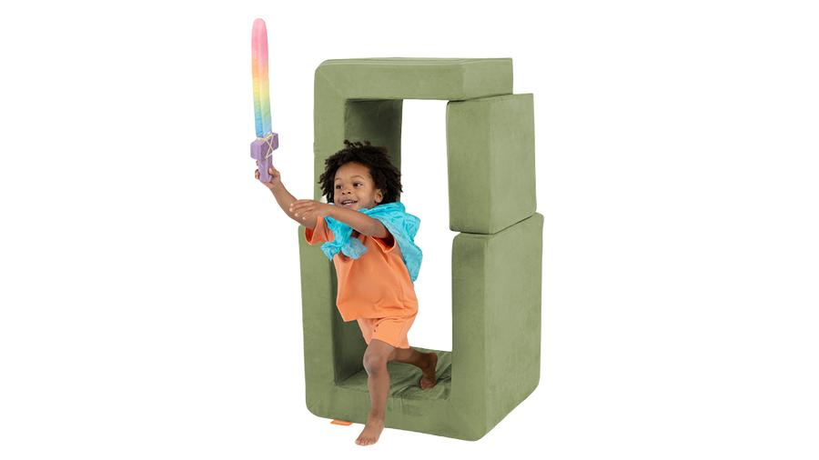 A child saves a foam sword and steps from a portal built from the pieces of a sage green Smore play chair. 