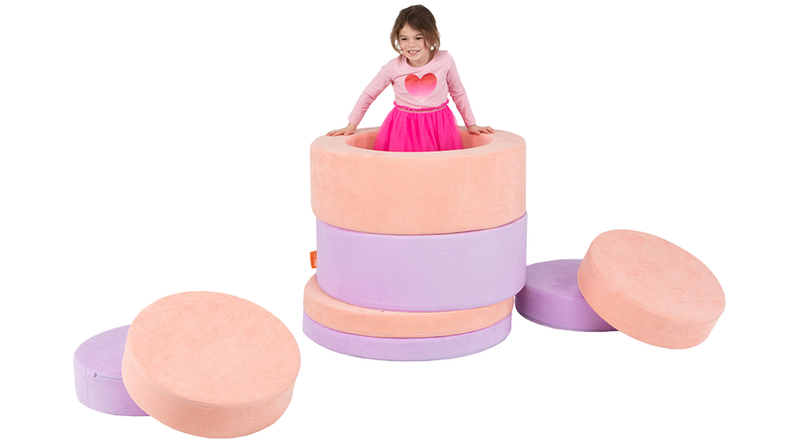 A child pops out of a tower constructed with the pieces of two Chunk play ottomans. 