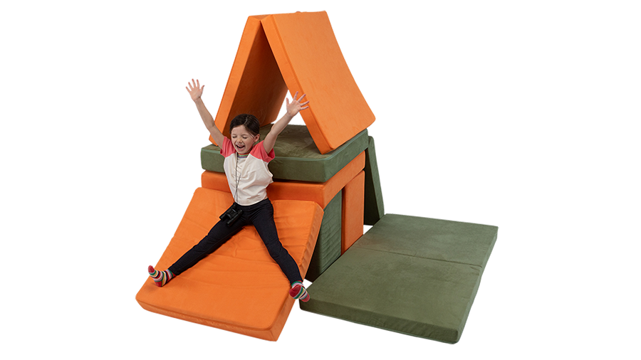 A child slides down a Nugget cushion, built into a two-Nugget fort constructed with two play couches.