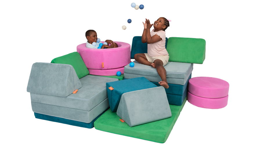 Two children laugh and sit on a play furniture build, made from three Nugget play couches and one Chunk play ottoman. 