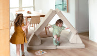 Two children run in circles around a Dunebuggy vintage beige play couch by Nugget, set up as a tunnel.