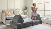 A child poses and sings on a Harbor charcoal gray play couch by Nugget, set up as a stage.